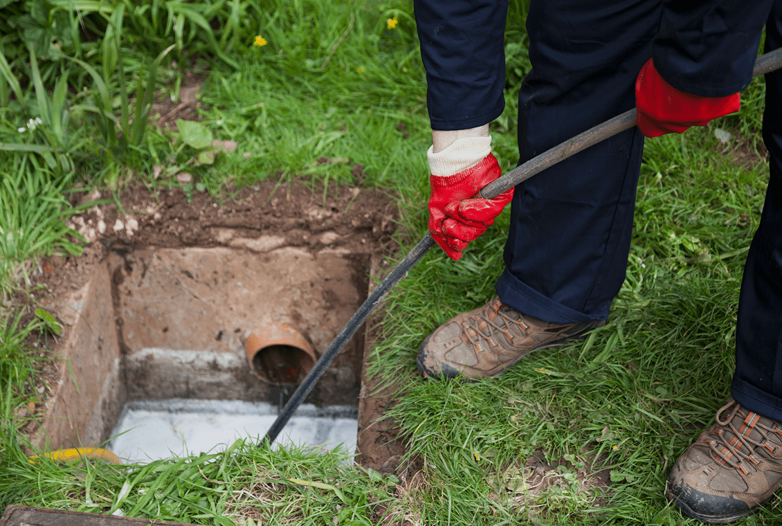 Person unclogging drain pipe outdoors
