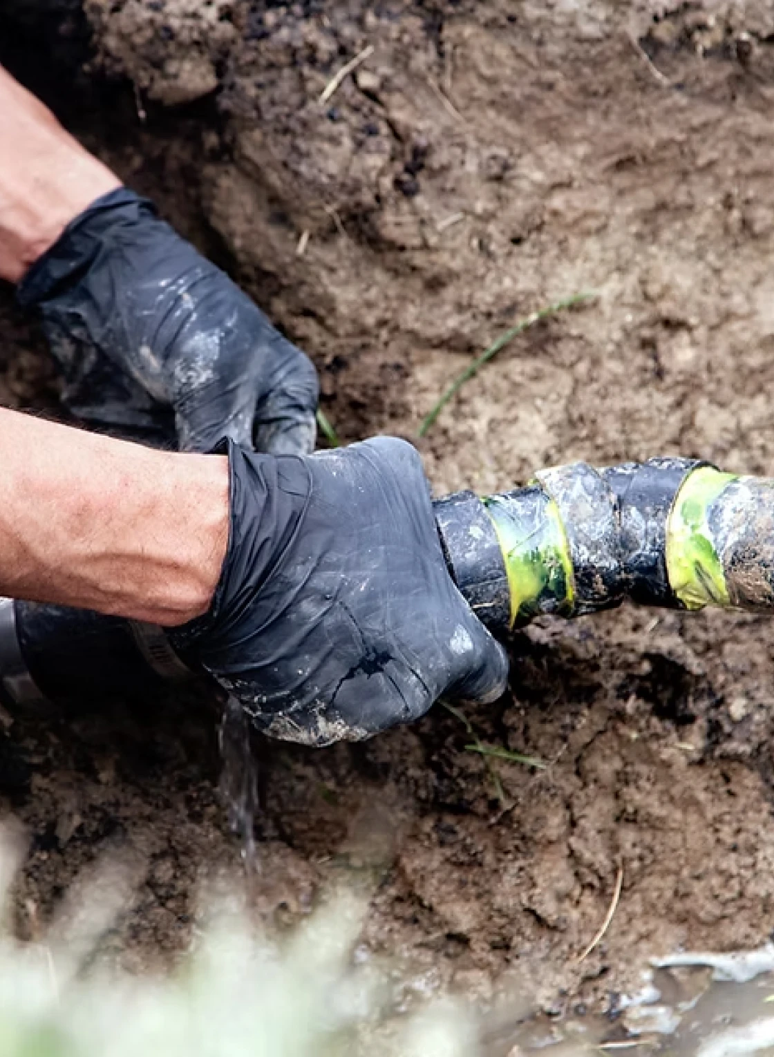 Black-gloved hands fixing outdoor plumbing