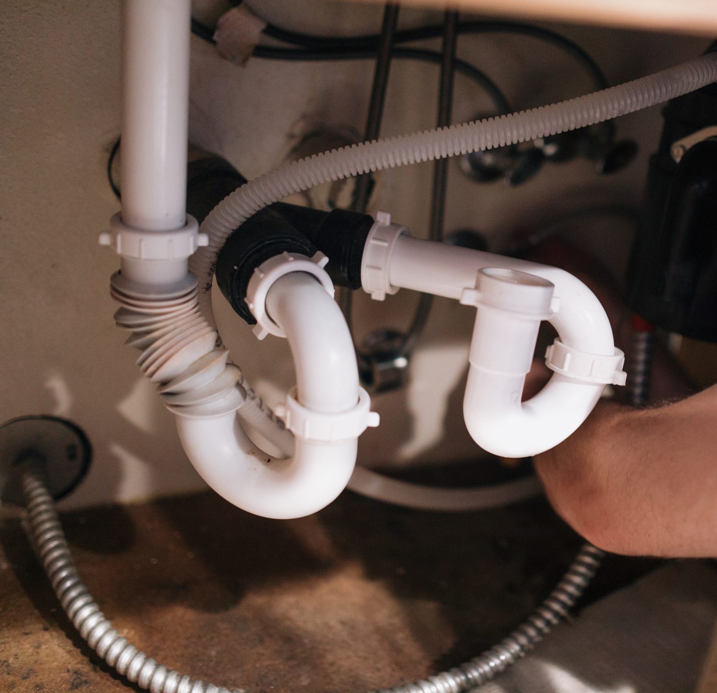 A Caucasian plumber works under a faucet sink to connect the drain pipes properly.